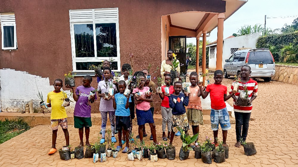 Eine Gruppe Kinder steht vor dem Waisenhaus und zeigt die Pflanzen, die sie einpflanzen wollen.